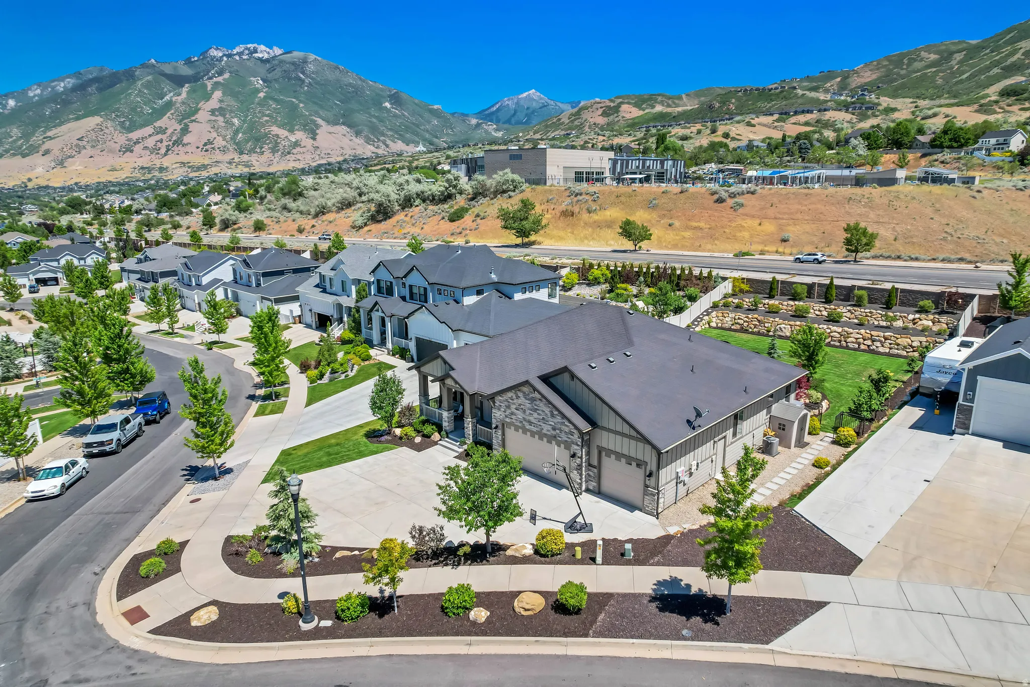 Contemporary residence featuring a two-car garage, stone and siding exterior, a landscaped front yard with mature trees, and a spacious backyard with terraced landscaping