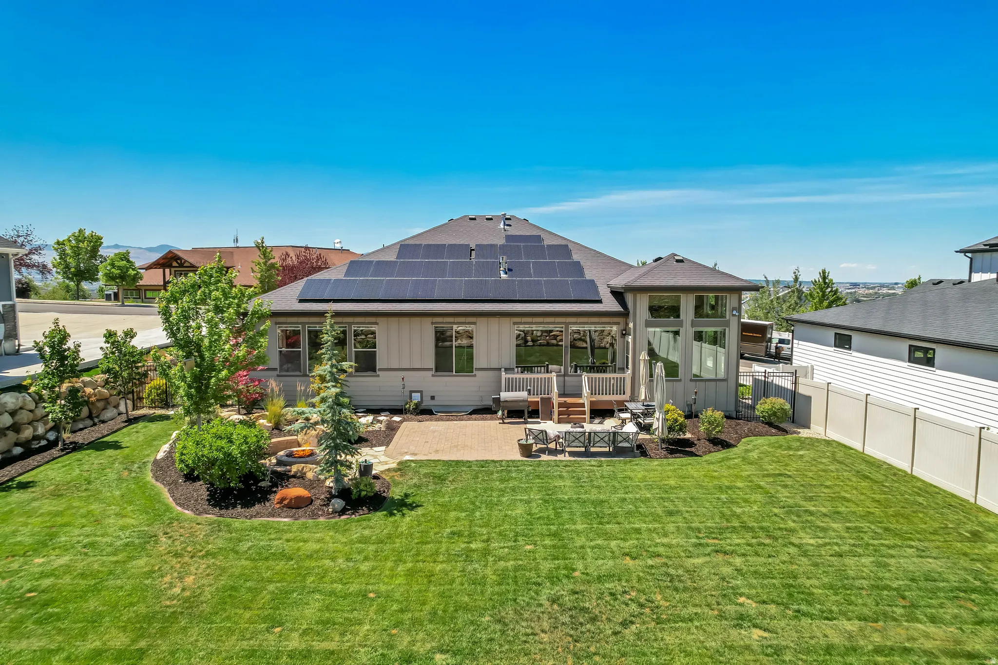 Rear exterior featuring solar panels, a multi-level deck, and a stone patio