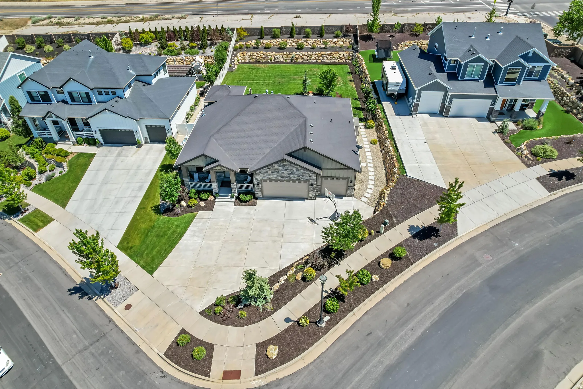 Corner lot property featuring a large concrete driveway, two-car garage, and mature landscaping