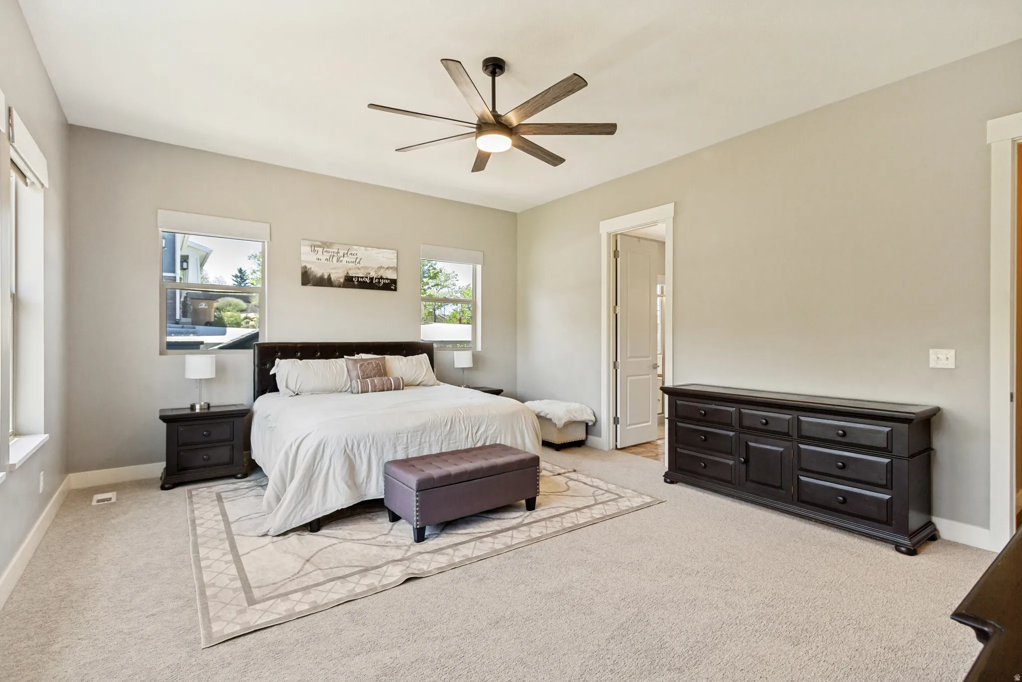 Spacious room featuring neutral carpeting, light gray walls, a ceiling fan with integrated lighting, and multiple windows