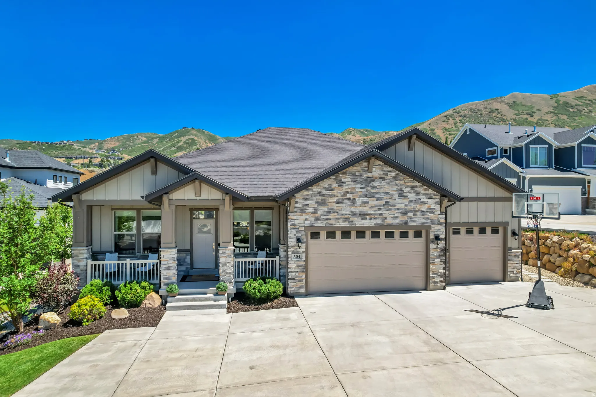 Ranch-style residence featuring stone and board-and-batten siding, a covered front porch, an attached three-car garage, and a concrete driveway