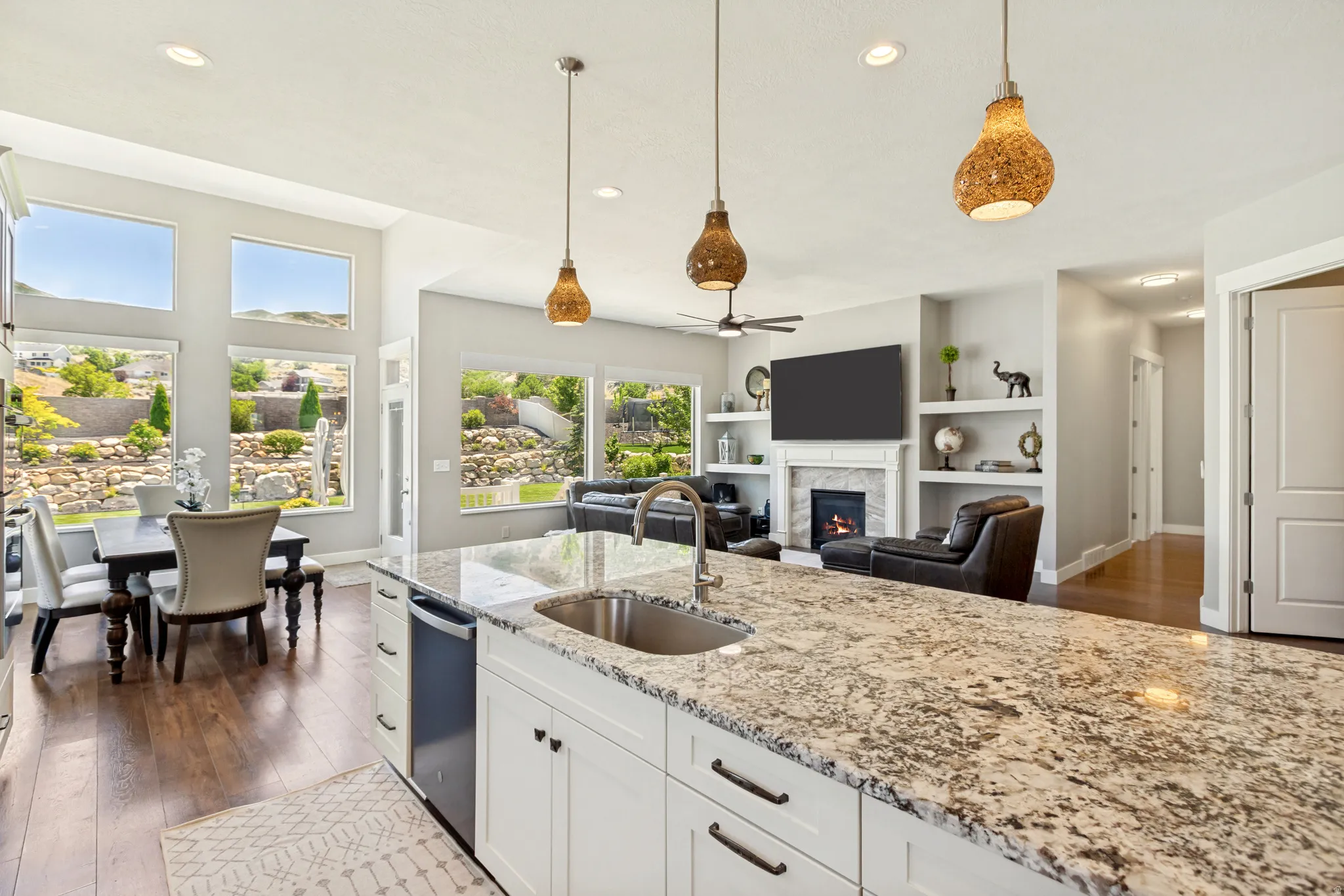 Open-concept kitchen and living area featuring a large island with a stainless steel sink, granite countertops, and white cabinetry