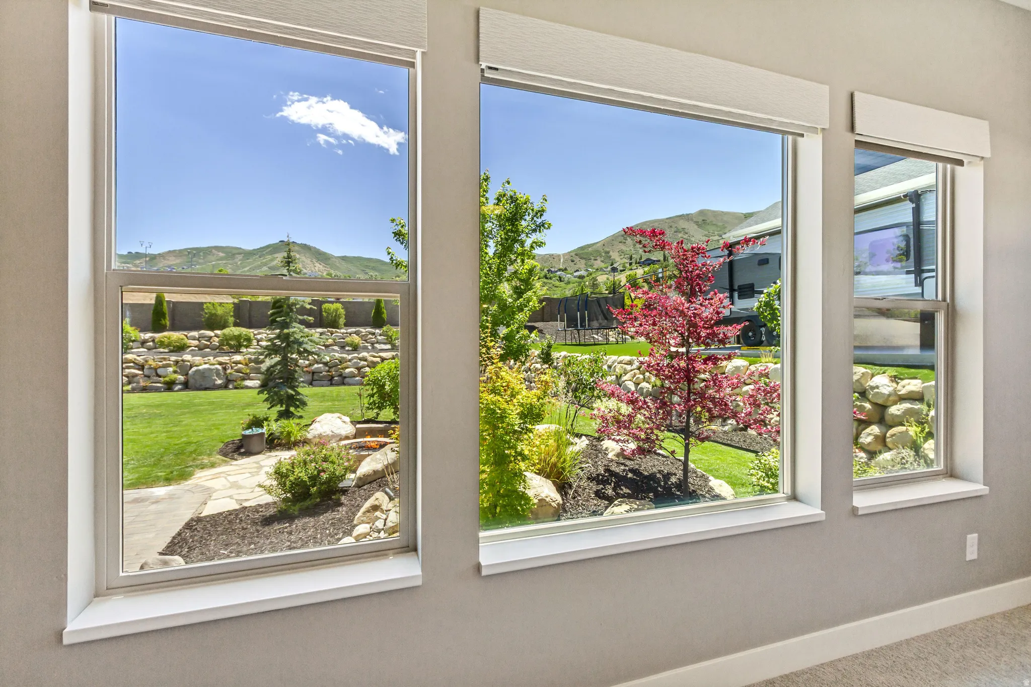 Multiple large windows with white trim, offering expansive views of a landscaped backyard