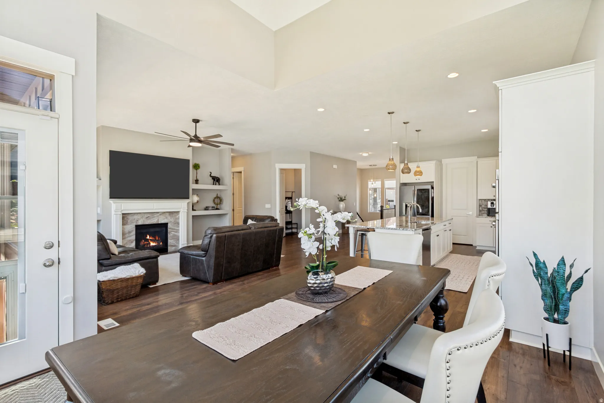 Open-concept living space featuring wood-finish flooring, a central fireplace with a stone surround, recessed lighting, and a kitchen island with pendant lighting