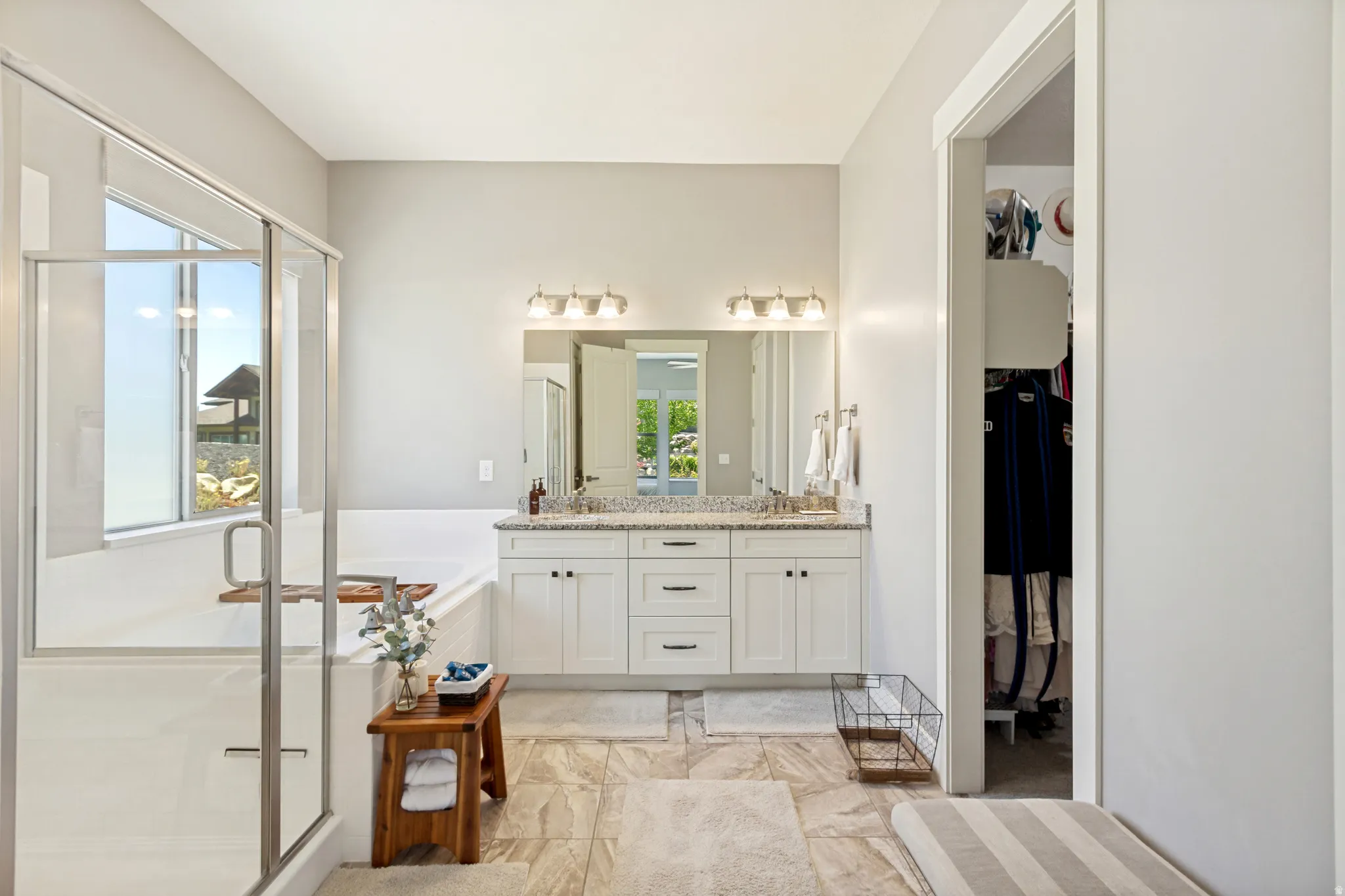 Spacious bathroom featuring a glass-enclosed shower, a separate soaking tub, a double vanity with ample counter space, custom white cabinetry, and large format floor tiling