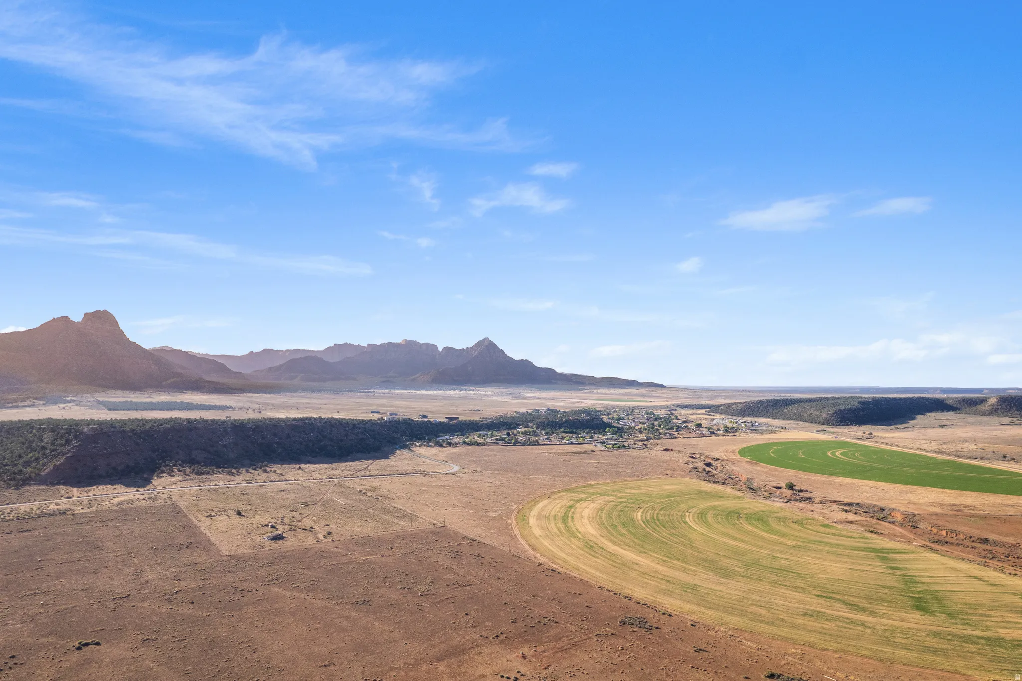 Expansive desert landscape featuring distant mountain ranges, a central village, and circular agricultural fields