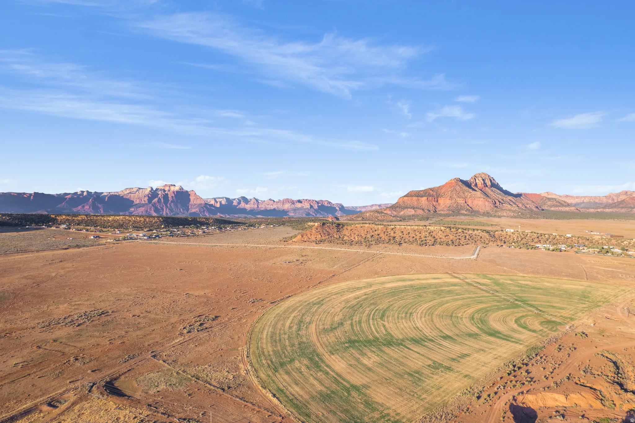 Expansive desert landscape featuring a circular irrigated field, surrounding arid terrain, and distant reddish-brown mountains under a clear sky