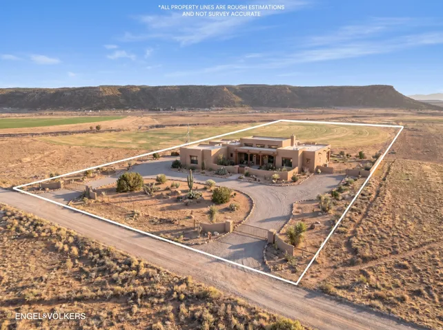 Adobe-style residence featuring a gravel circular driveway, mature desert landscaping, and a secure gated entrance