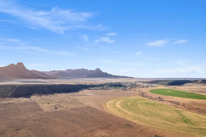 Expansive desert landscape featuring distant mountain ranges, a central village, and circular agricultural fields