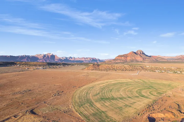 Expansive desert landscape featuring a circular irrigated field, surrounding arid terrain, and distant reddish-brown mountains under a clear sky