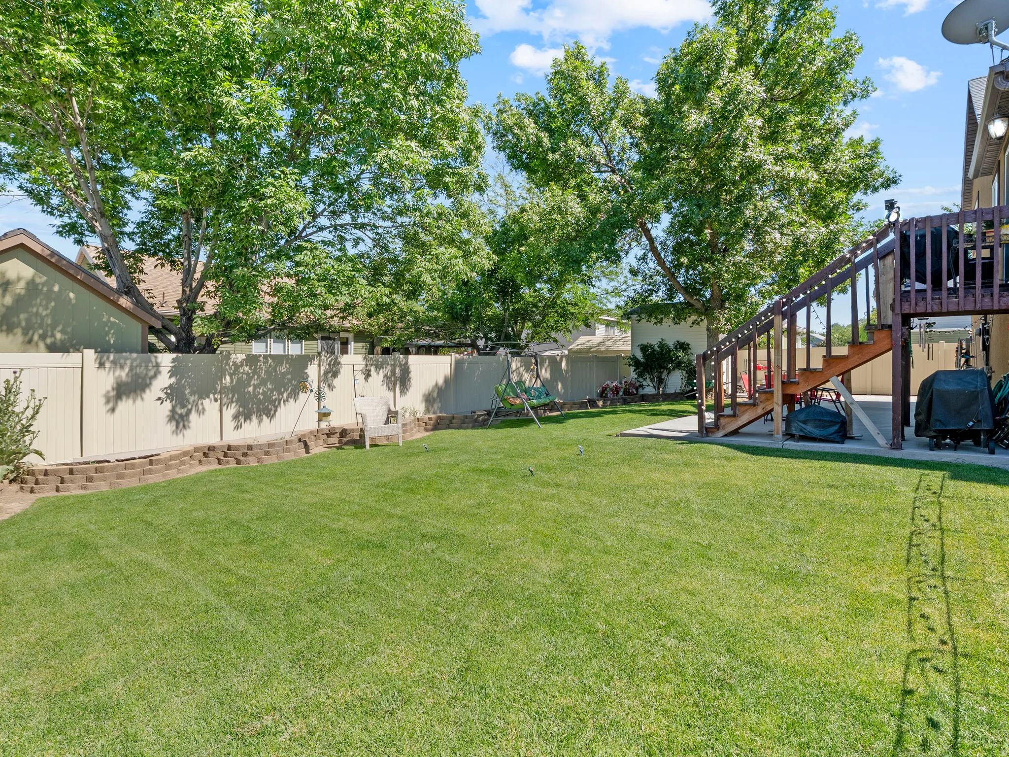 Expansive backyard featuring a lush lawn, mature trees, a multi-level deck with stairs, a concrete patio, and privacy fencing