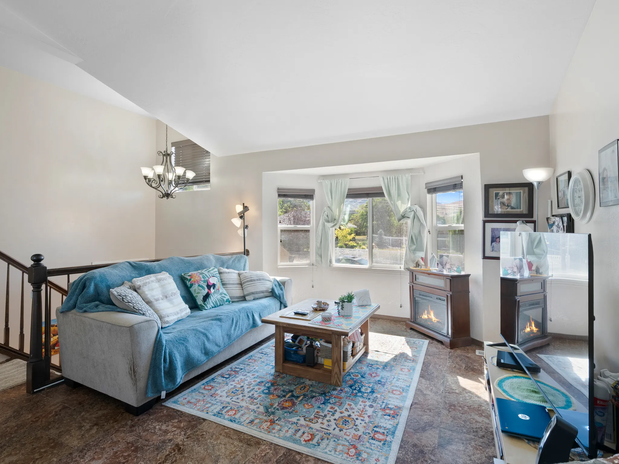 Living area featuring high ceilings, bay windows, wood-finish flooring, a contemporary chandelier, and a dark wood staircase with spindle railings