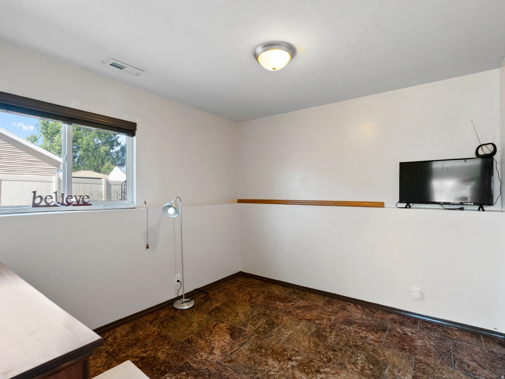 Room featuring a window with a dark roller shade, textured walls with a chair rail, and patterned flooring
