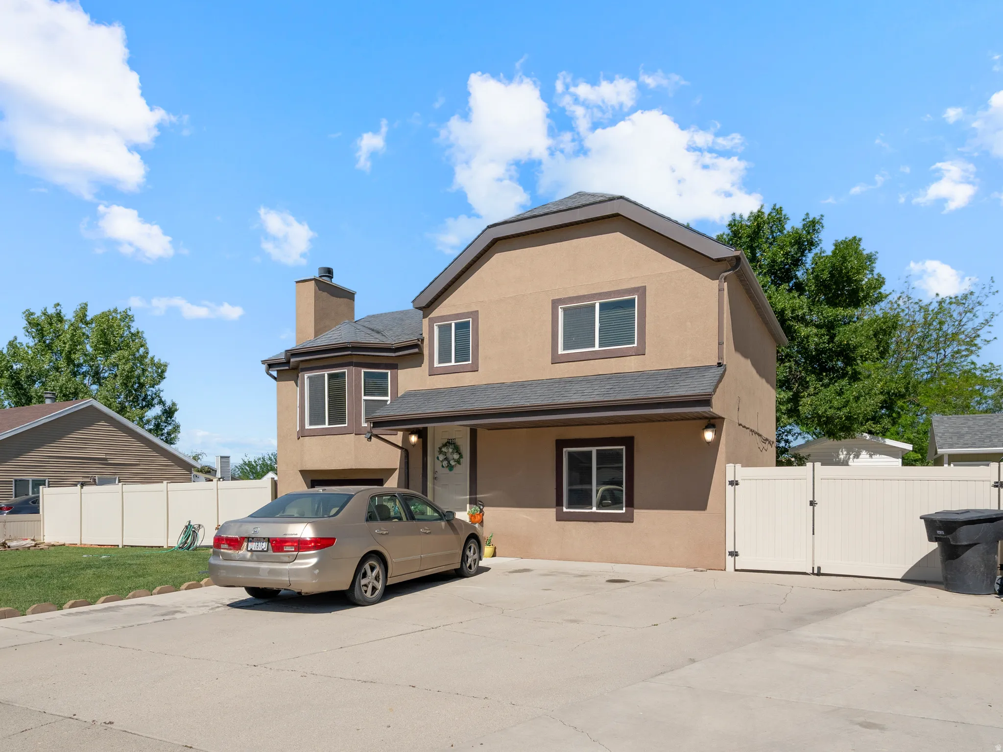 Two-story stucco exterior featuring a bay window, dark shingles, white-framed windows, and a concrete driveway