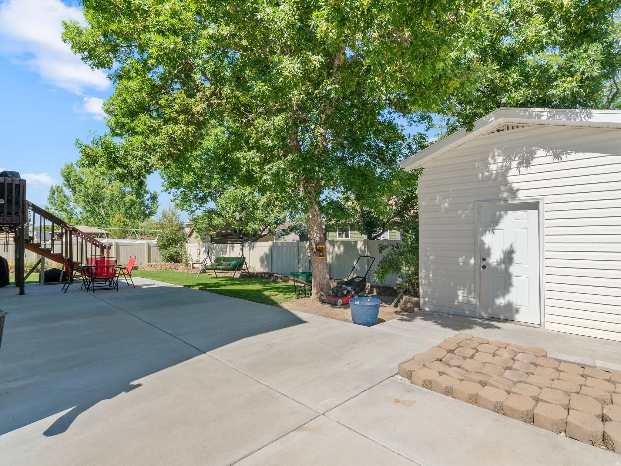 Spacious backyard featuring a large concrete patio, mature shade tree, and a storage shed with horizontal siding