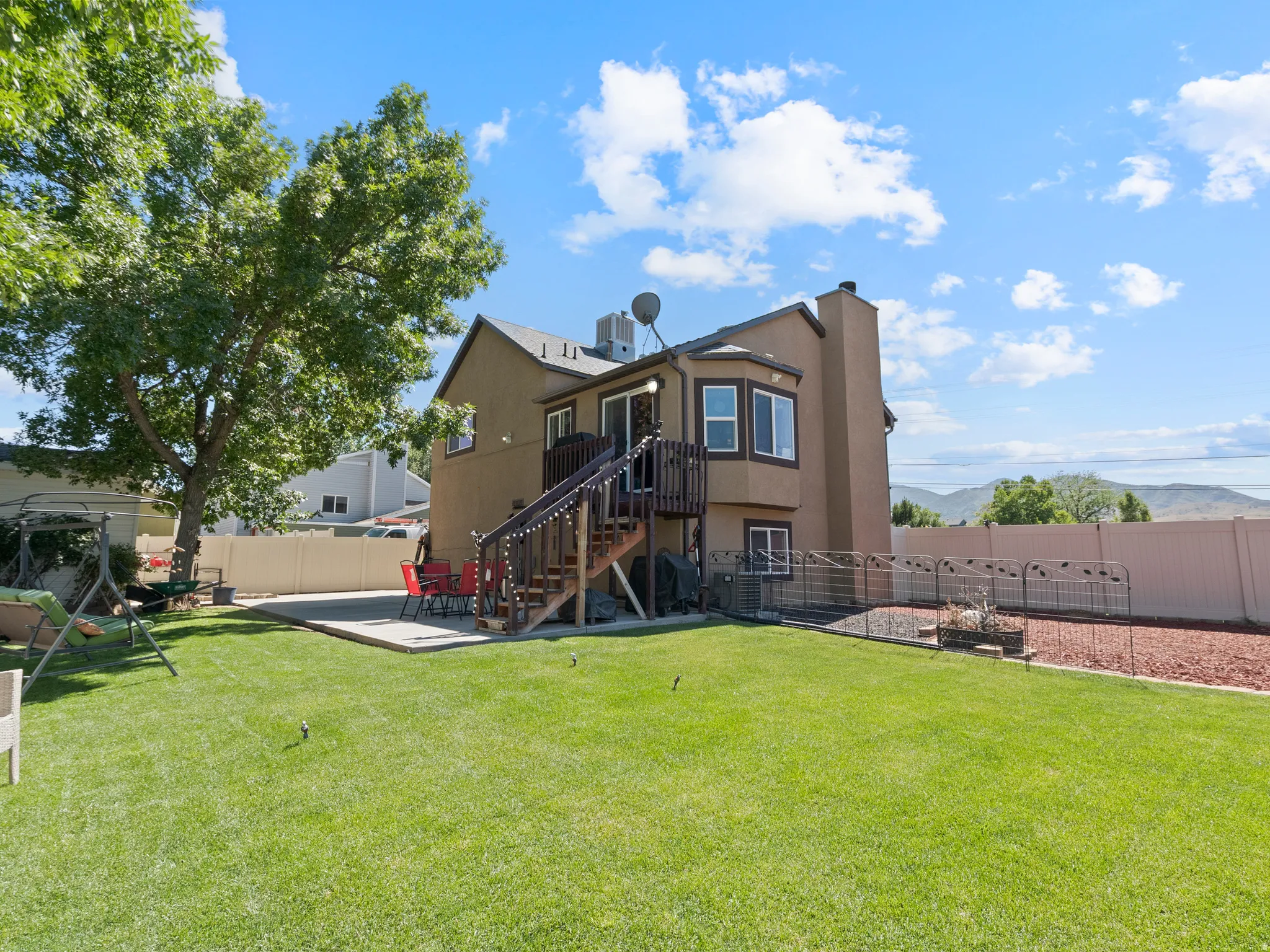 Expansive green lawn with a large shade tree, concrete patio, and a two-story residence featuring a bay window