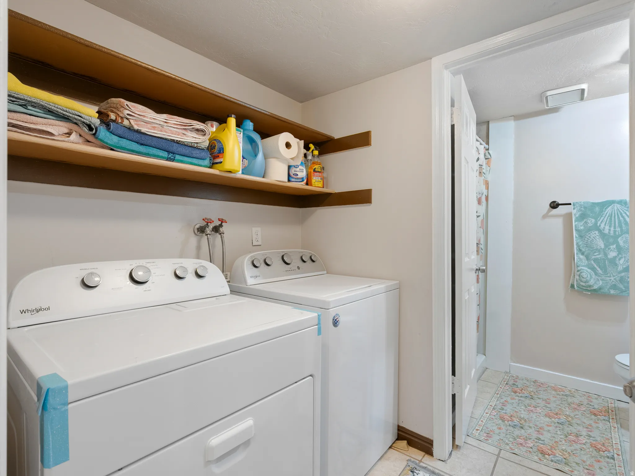 Dedicated laundry area featuring a white washer and dryer, wood-finish shelving, and neutral wall paint
