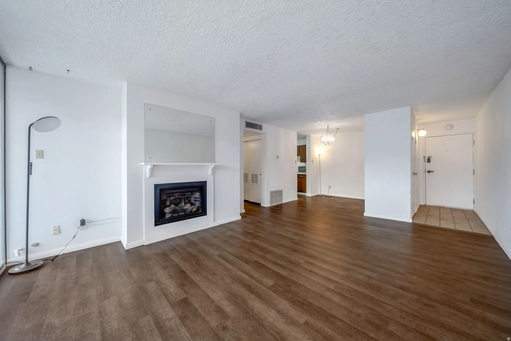 Spacious living area featuring wood-finish flooring, a fireplace with a white mantel, and a large wall-mounted mirror