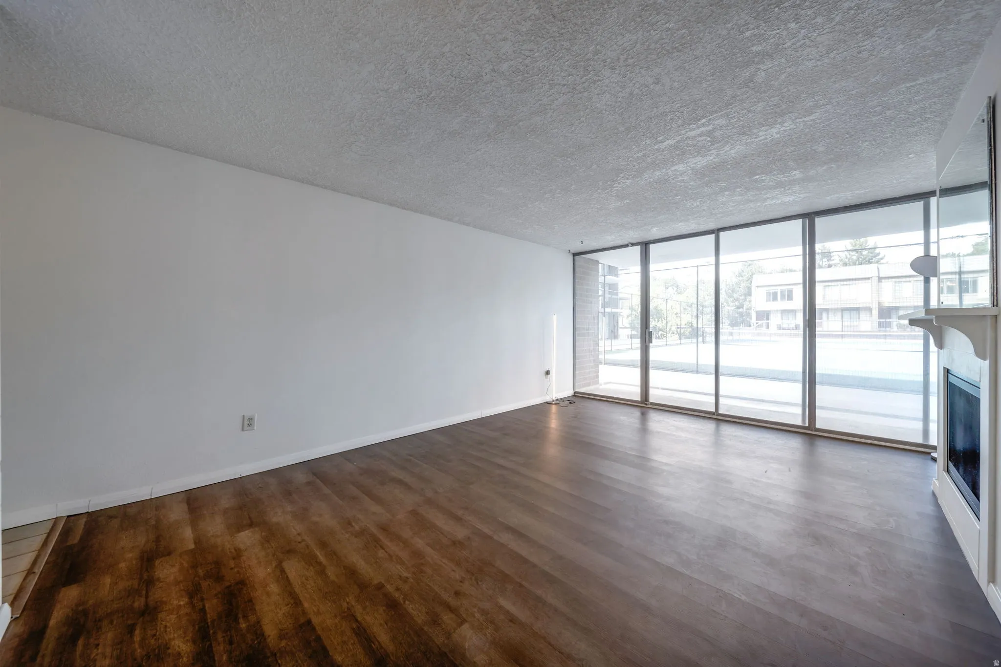 Spacious interior featuring wood-finish flooring, a white mantel fireplace, and a wall of floor-to-ceiling windows