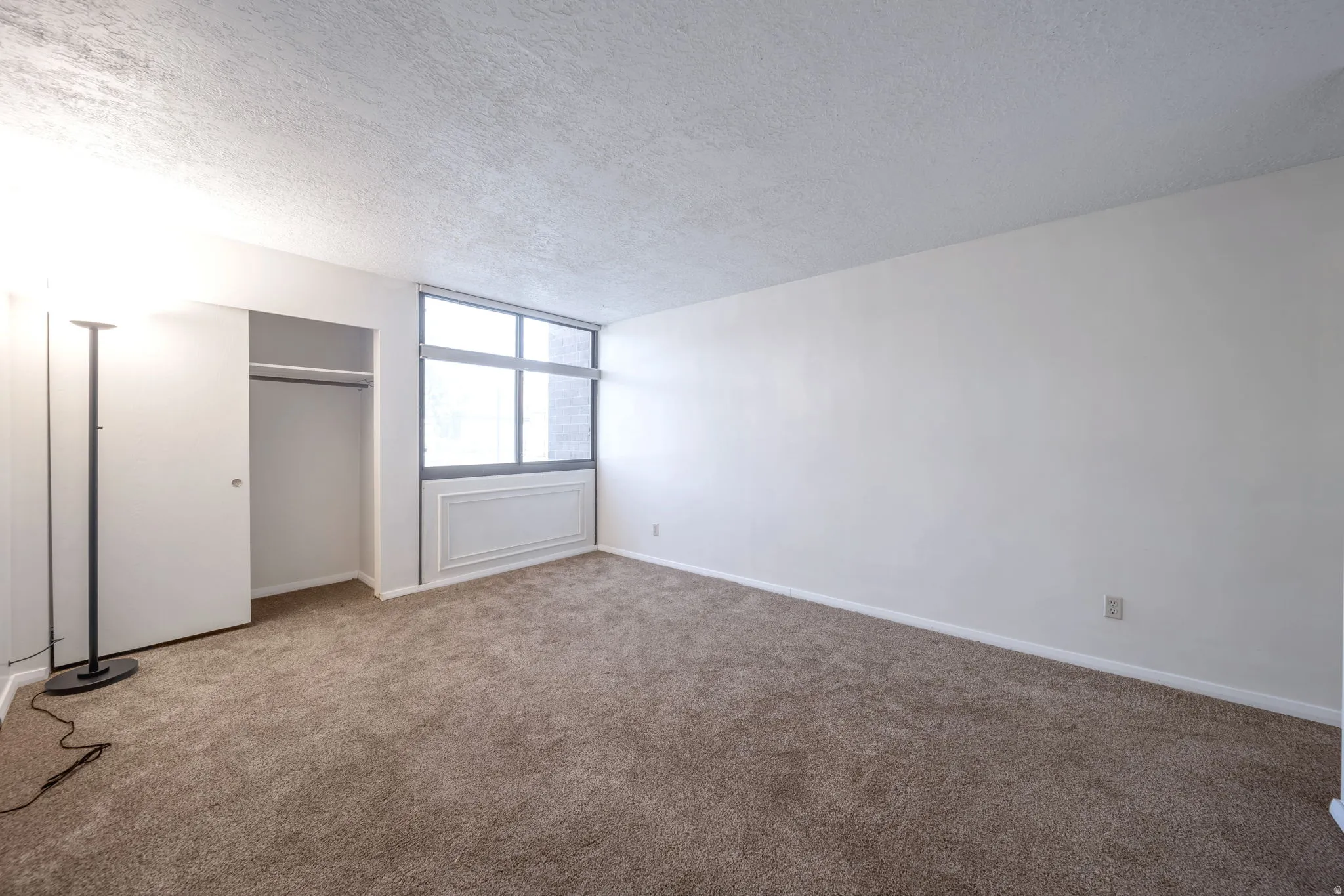 Carpeted room featuring a large window, a built-in closet with bi-fold doors, white baseboards, and neutral wall finishes