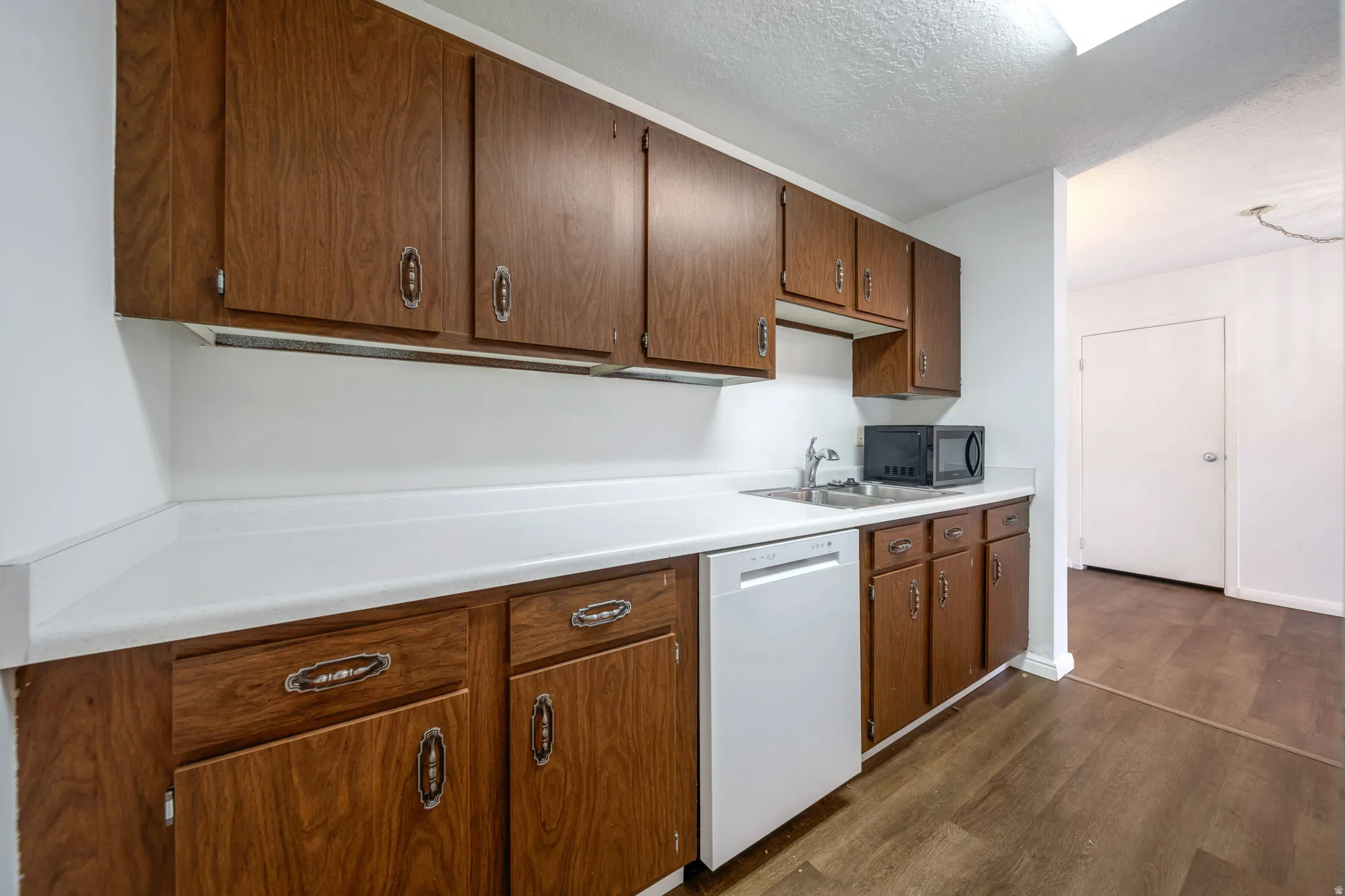 Kitchen featuring wood-finish cabinetry, white countertops, and a stainless steel sink with a chrome faucet