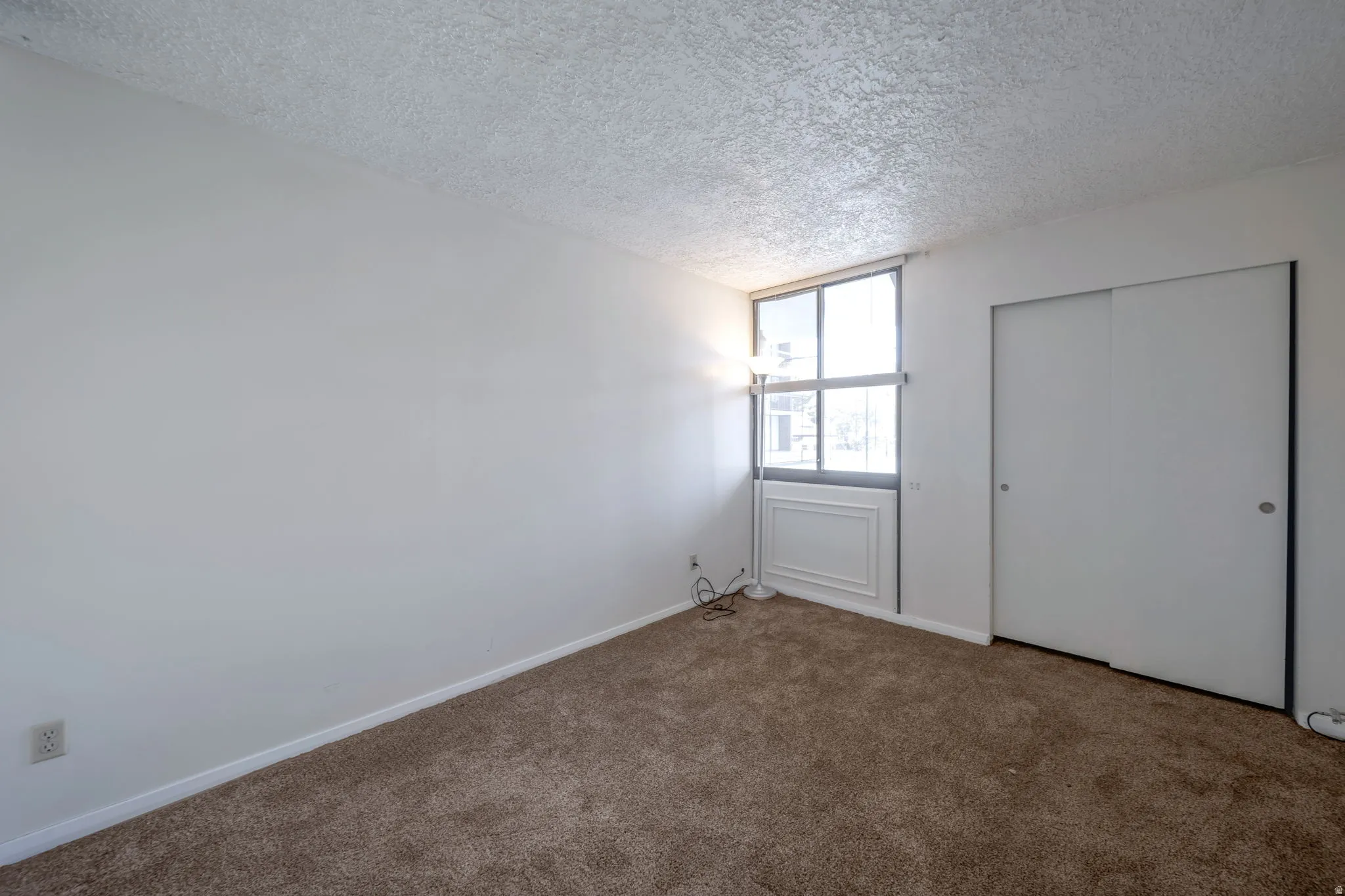Room featuring a large window with decorative paneling below, a neutral wall color, and wall-to-wall carpeting