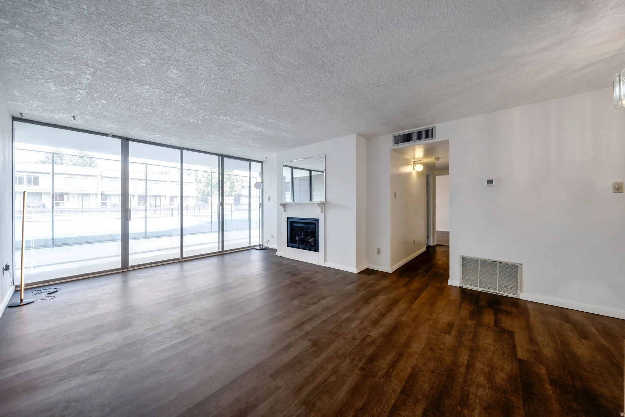 Spacious living area featuring extensive sliding glass doors, rich wood-finish flooring, a white mantel fireplace with a dark insert, a mirrored wall accent, and white painted walls