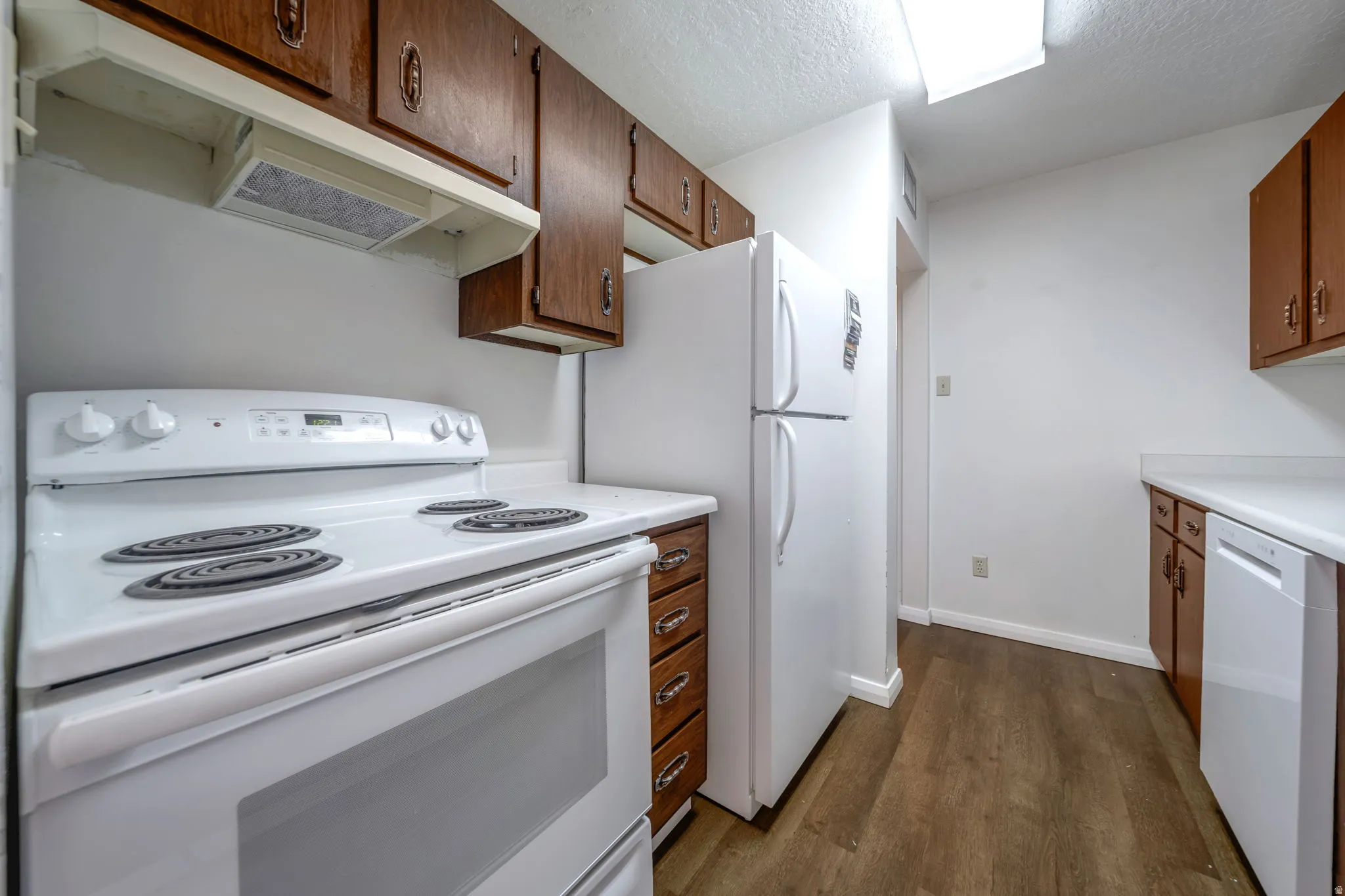 Kitchen featuring white appliances, wood-finish flooring, wood cabinetry, and white countertops