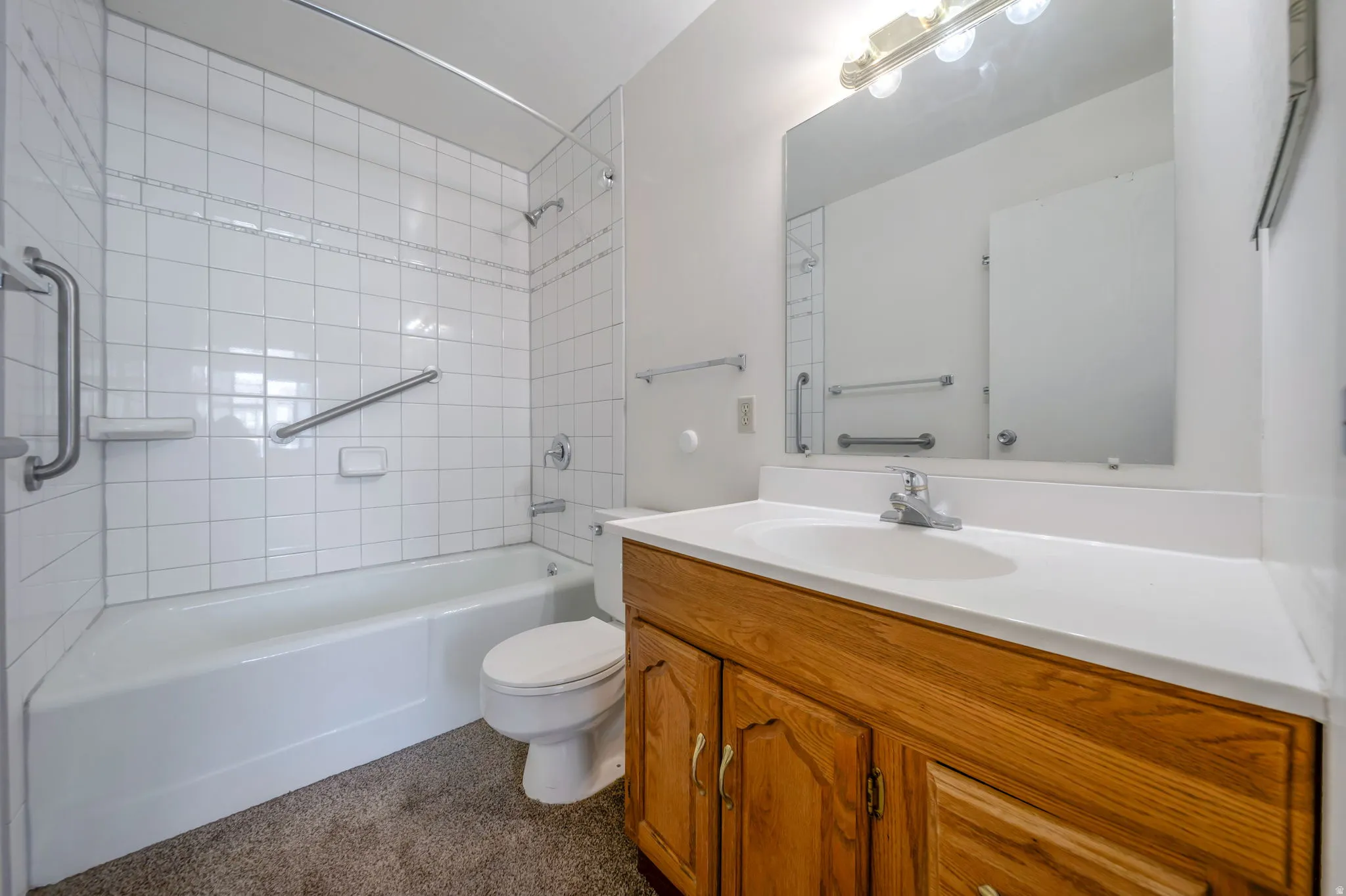 Bathroom featuring a white bathtub, tiled shower surround, and a wood-finish vanity with an integrated sink and mirror