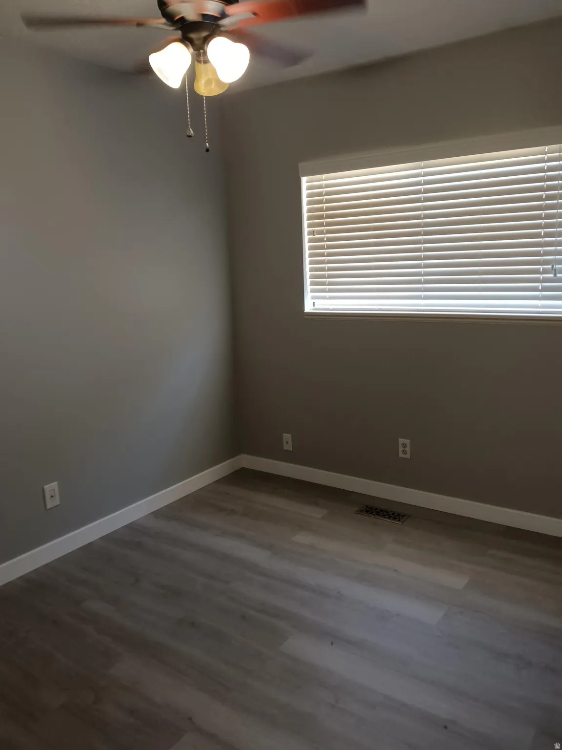 Room featuring wood-finish flooring, a ceiling fan with integrated lighting, a window with horizontal blinds, and a neutral wall color