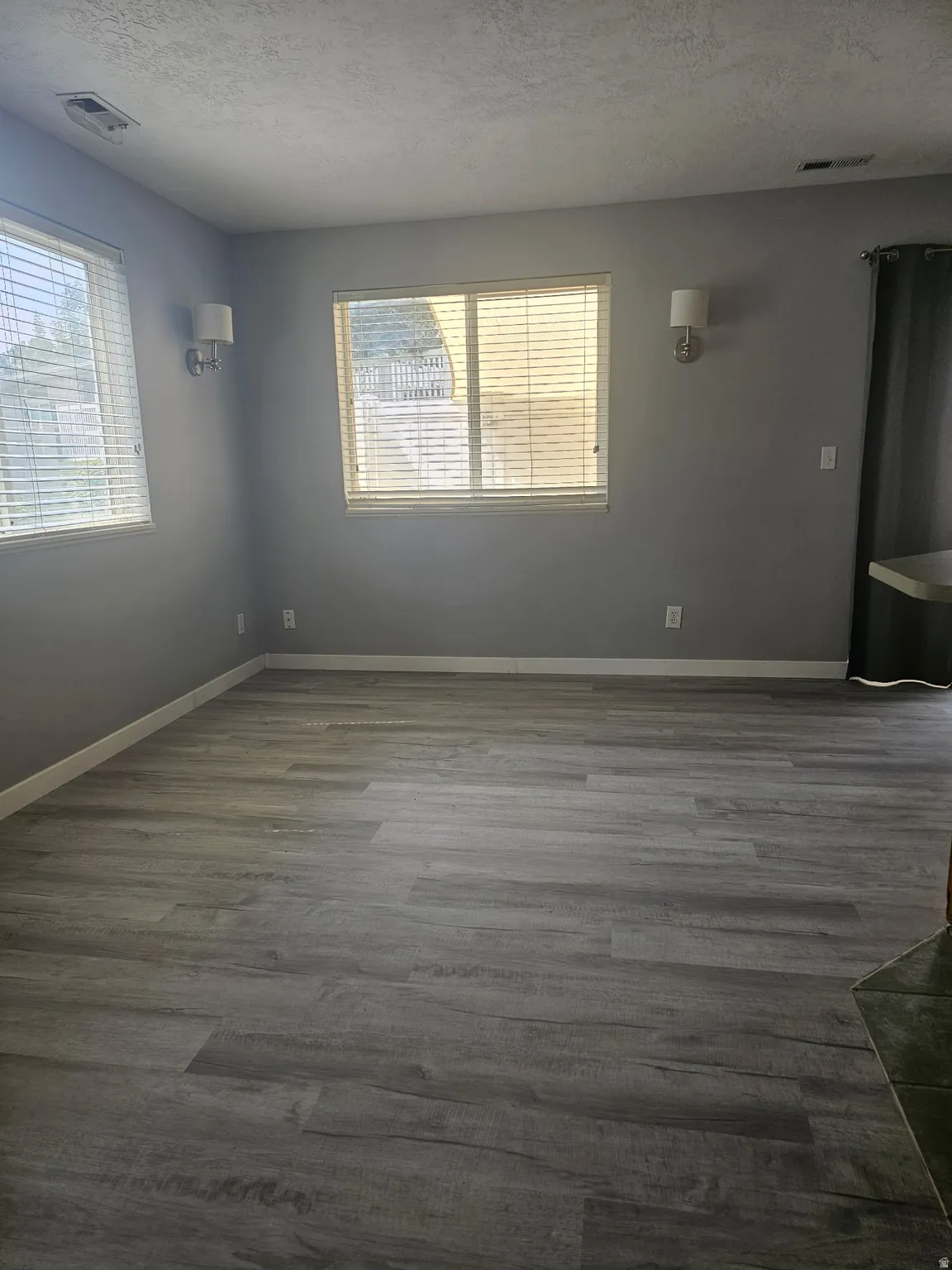 Wood-finish flooring, multiple windows with blinds, wall-mounted sconce lighting, and a tiled hearth