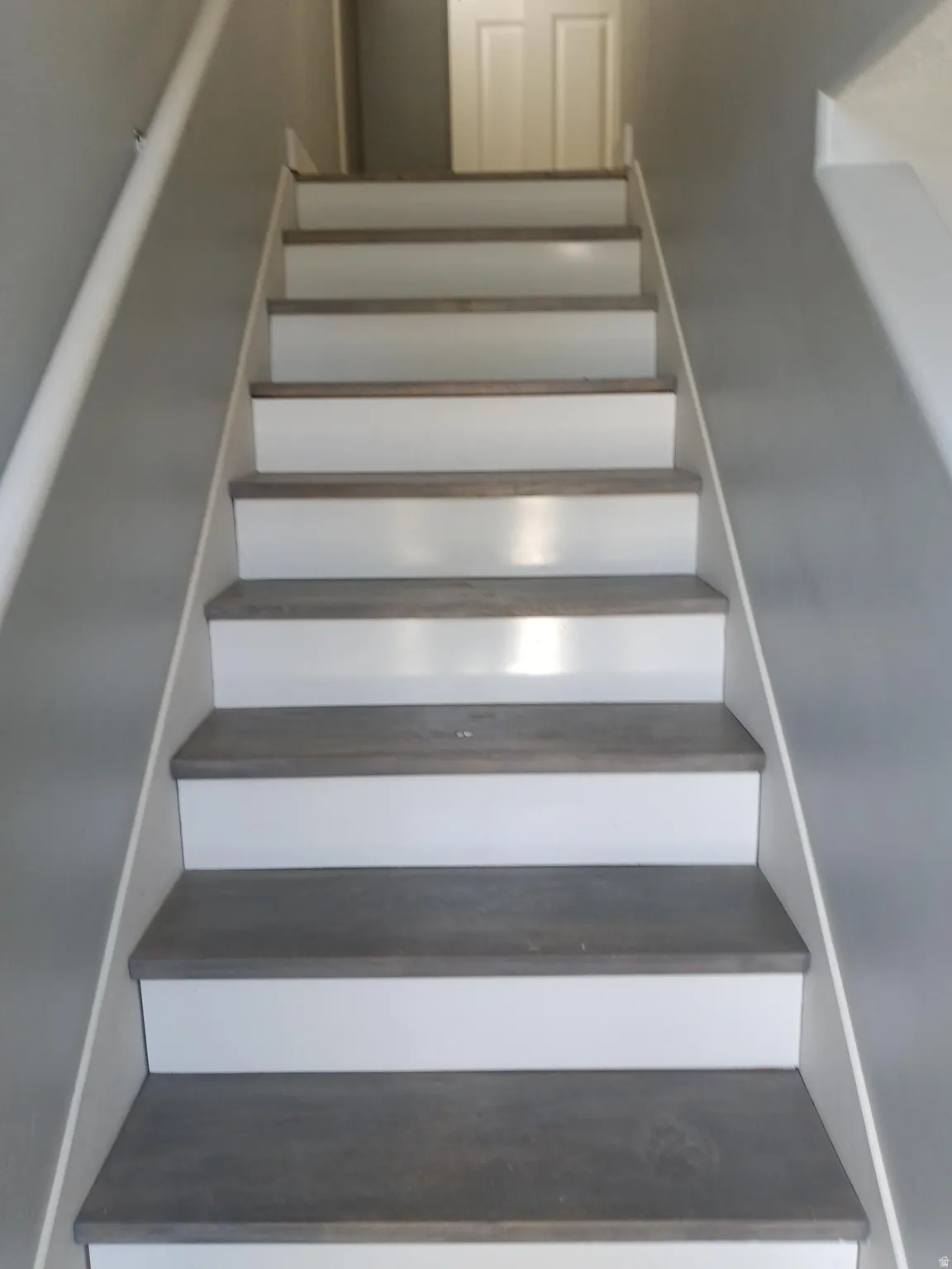 Staircase featuring wood-finish treads, white risers, and a contrasting handrail against gray walls