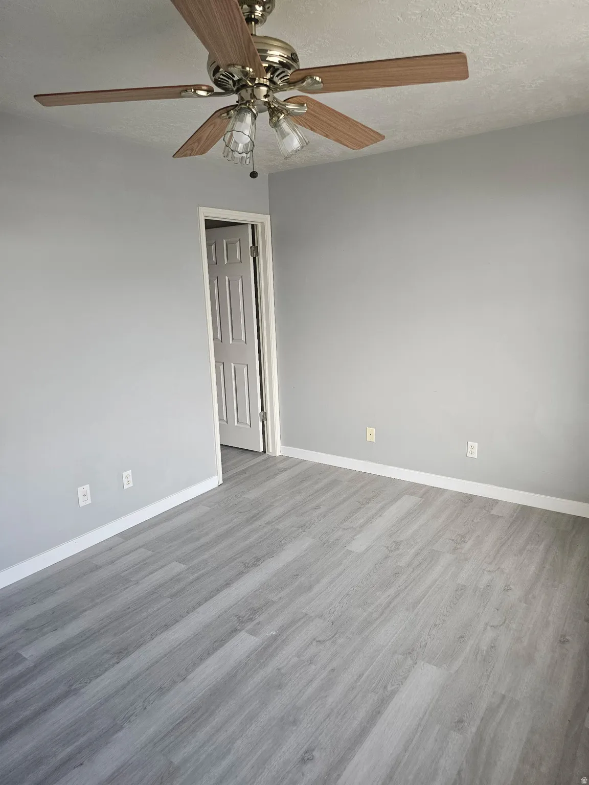 Room featuring light gray walls, wood-finish flooring, and a ceiling fan with integrated lighting