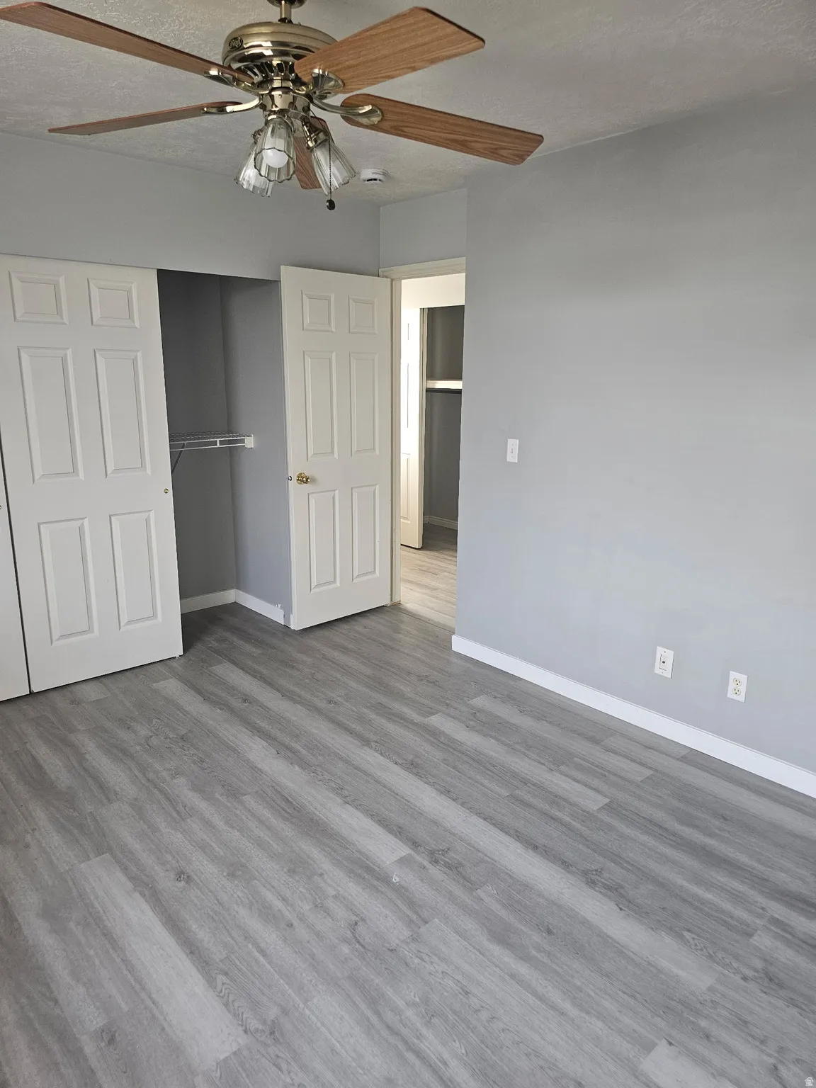 Wood-finish flooring, ceiling fan with light fixture, light gray wall finish, white baseboards, and white paneled doors