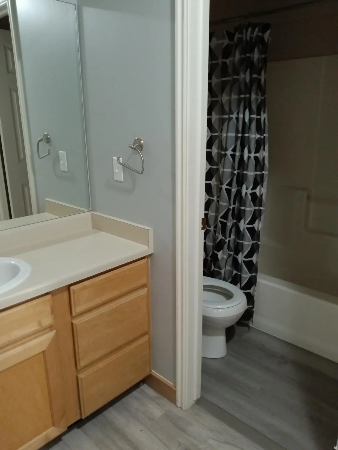 Bathroom featuring a light wood-finish vanity with an integrated sink, a light-toned countertop, a large wall-mounted mirror, brushed nickel hardware, and wood-finish flooring