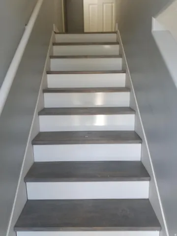 Staircase featuring wood-finish treads, white risers, and a contrasting handrail against gray walls