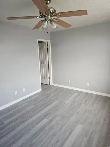 Room featuring light gray walls, wood-finish flooring, and a ceiling fan with integrated lighting