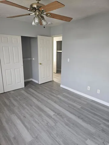 Wood-finish flooring, ceiling fan with light fixture, light gray wall finish, white baseboards, and white paneled doors