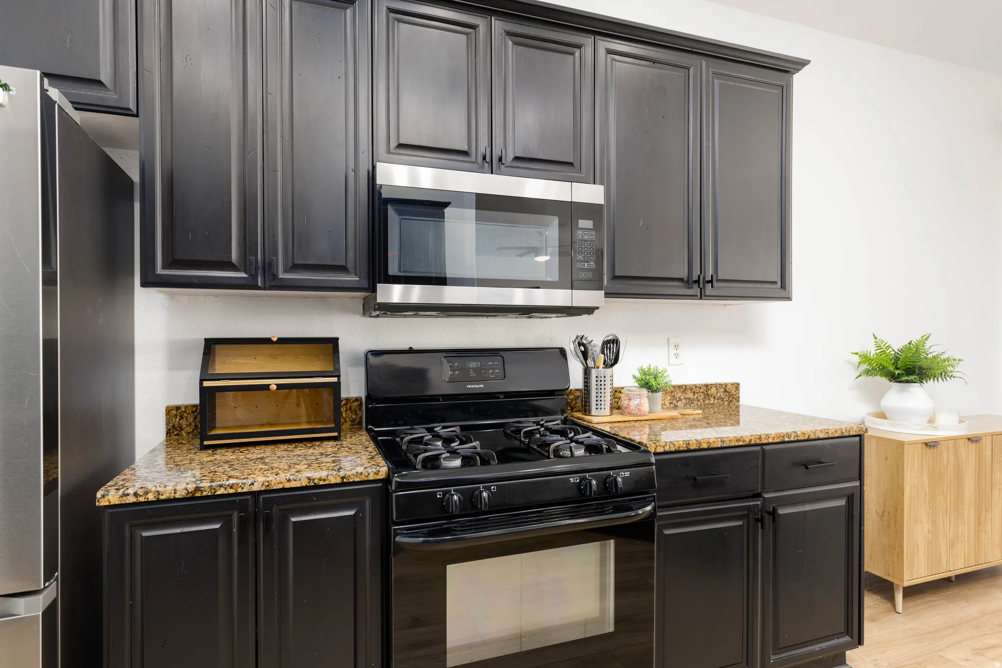 Kitchen featuring dark cabinetry, granite countertops, black gas range, and stainless steel microwave