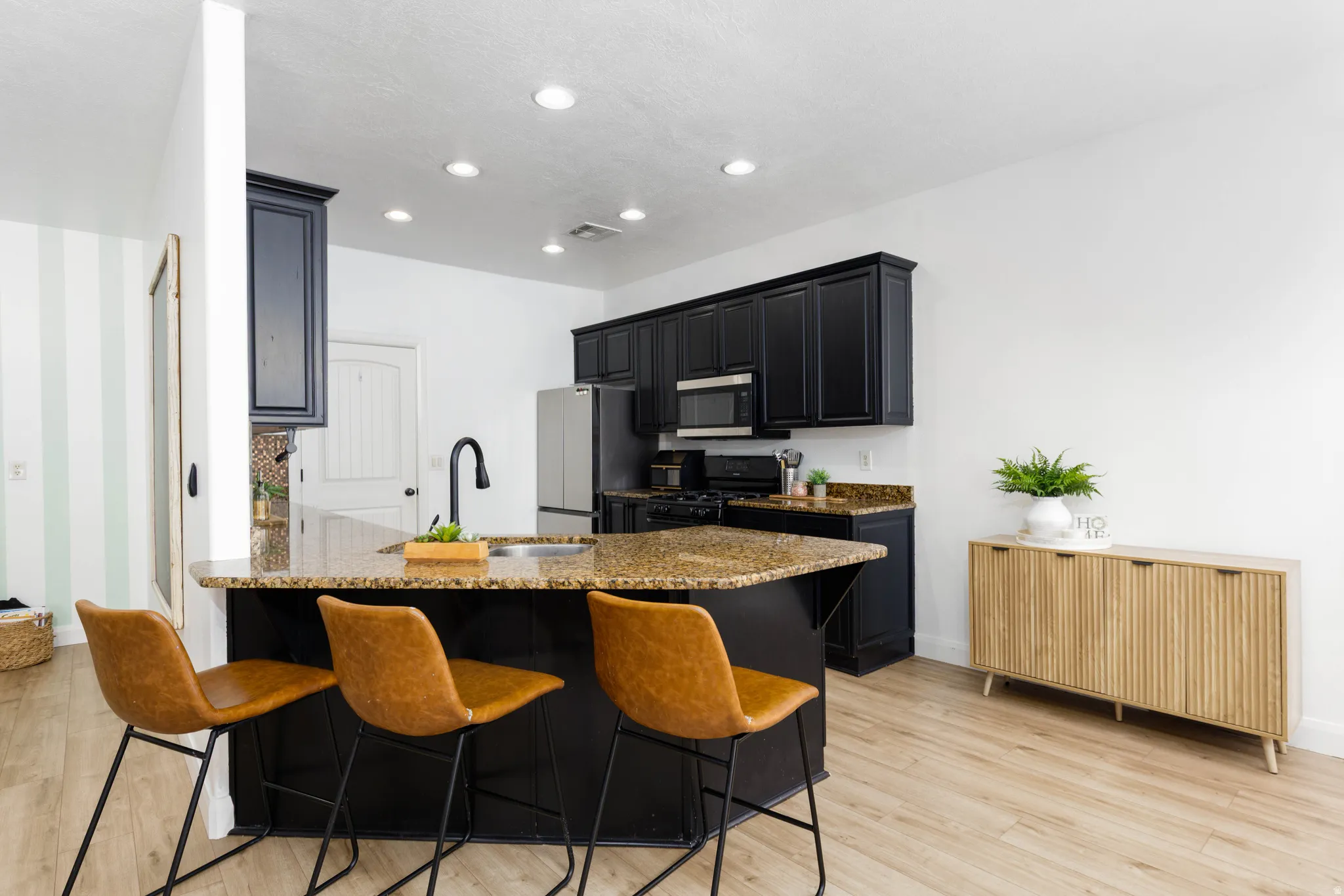 Open-concept kitchen featuring black cabinetry, granite countertops, stainless steel appliances, and wood-finish flooring