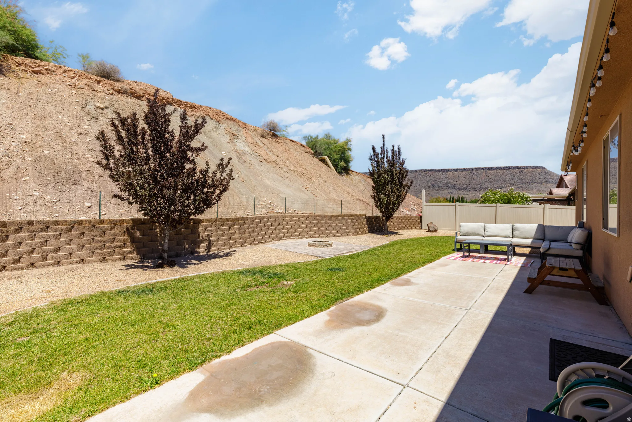 Expansive backyard featuring a concrete patio, green lawn, and terraced retaining wall
