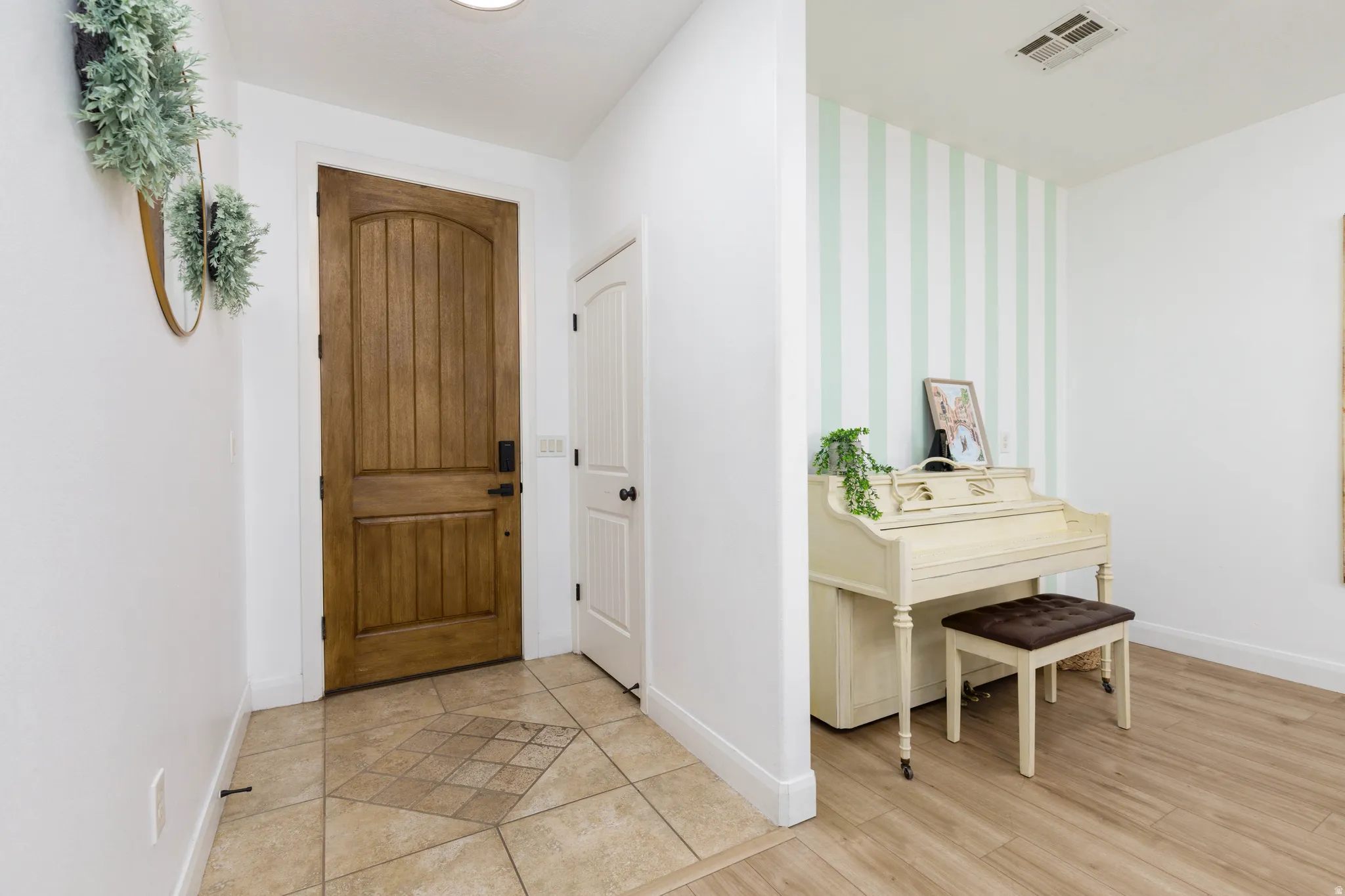 Entryway featuring a paneled wood door with dark hardware, tile flooring with a patterned inlay, and light wood-finish flooring extending into an adjacent area with accent wall