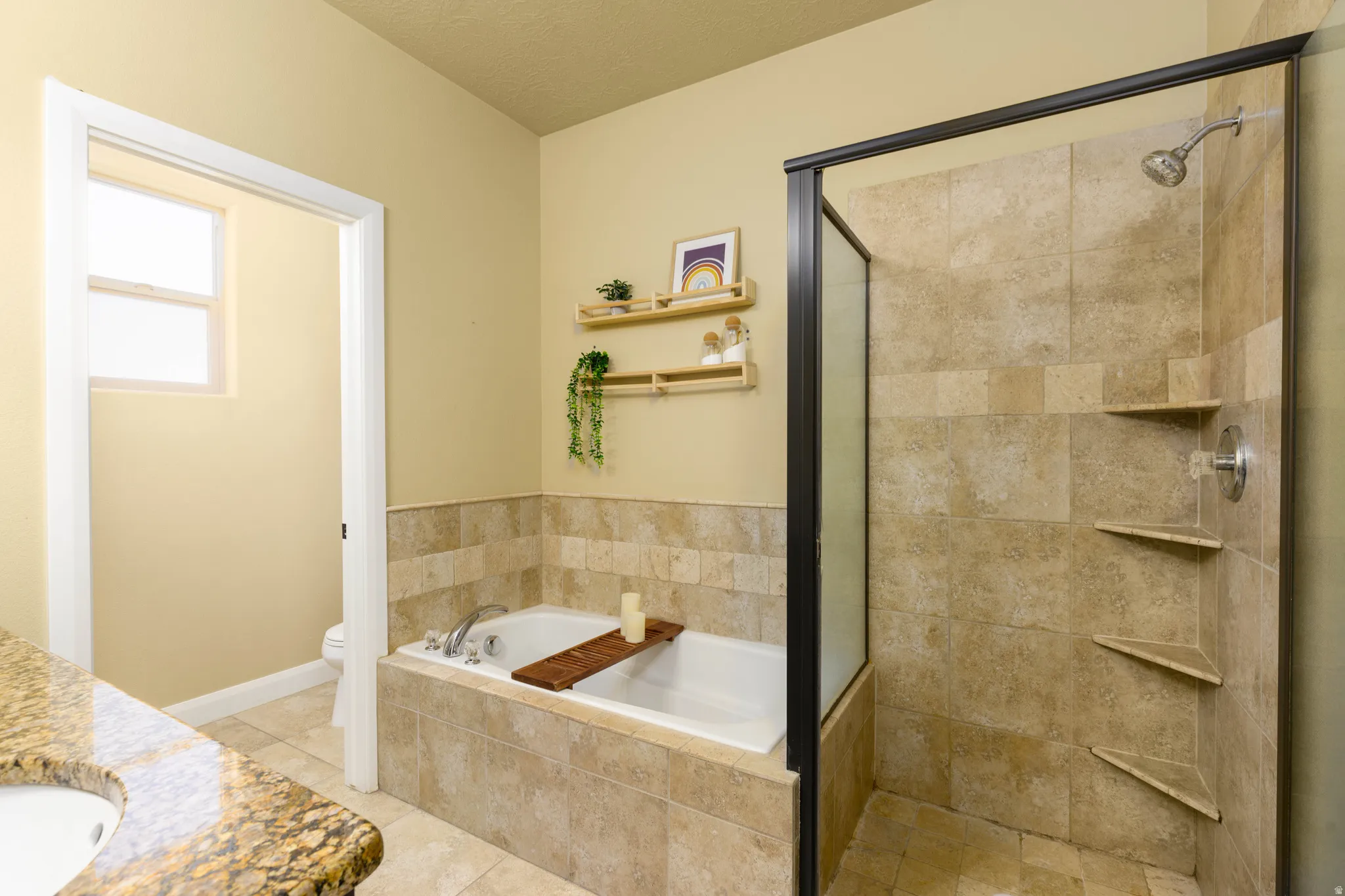 Primary suite bathroom featuring a built-in tub with tile surround, a separate shower enclosure with tile walls and integrated shelving, a granite-finish countertop, and tile flooring