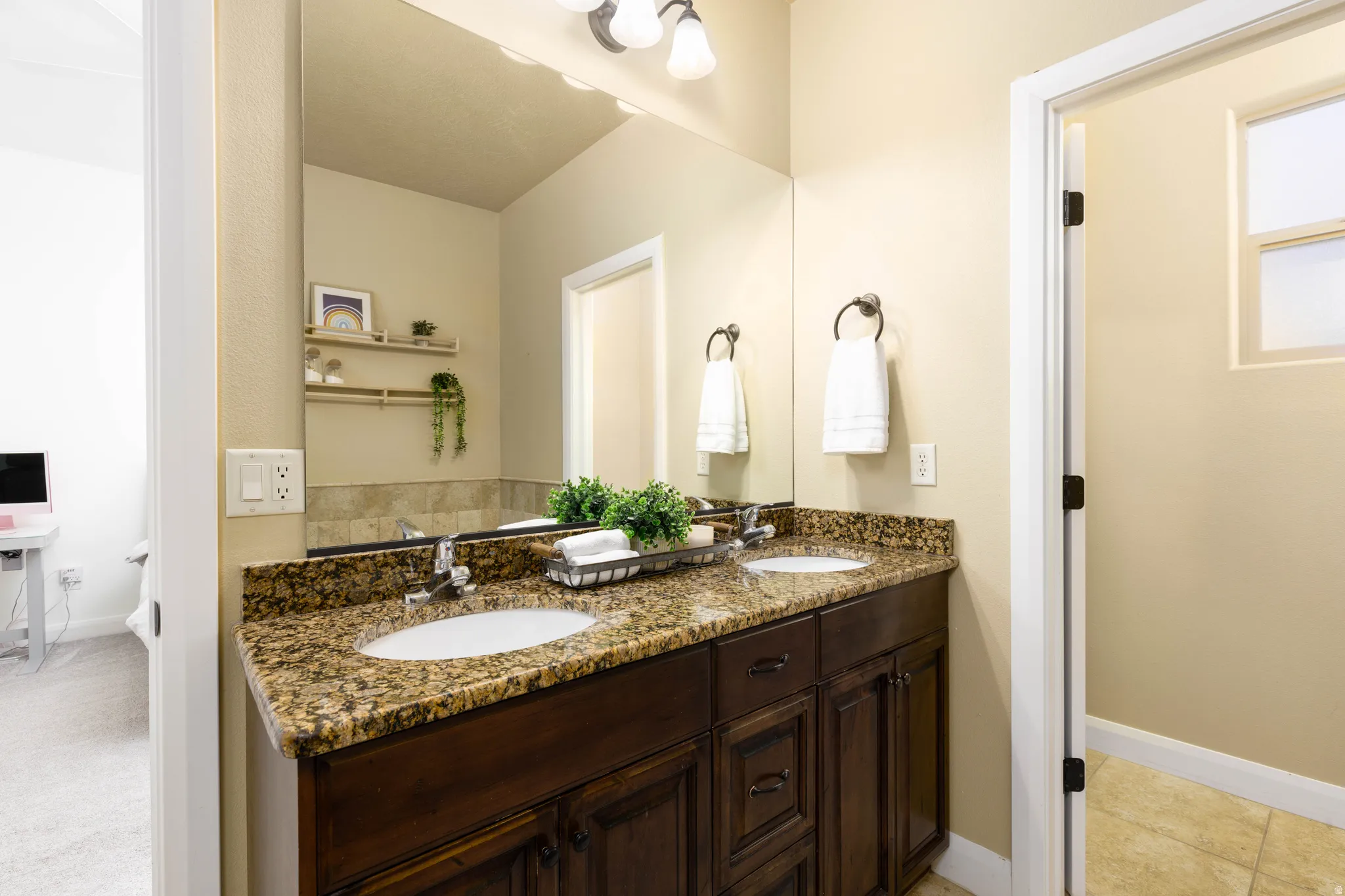 Primary suite bathroom featuring a dual sink vanity with a granite-style countertop, integrated sinks, and dark wood cabinetry