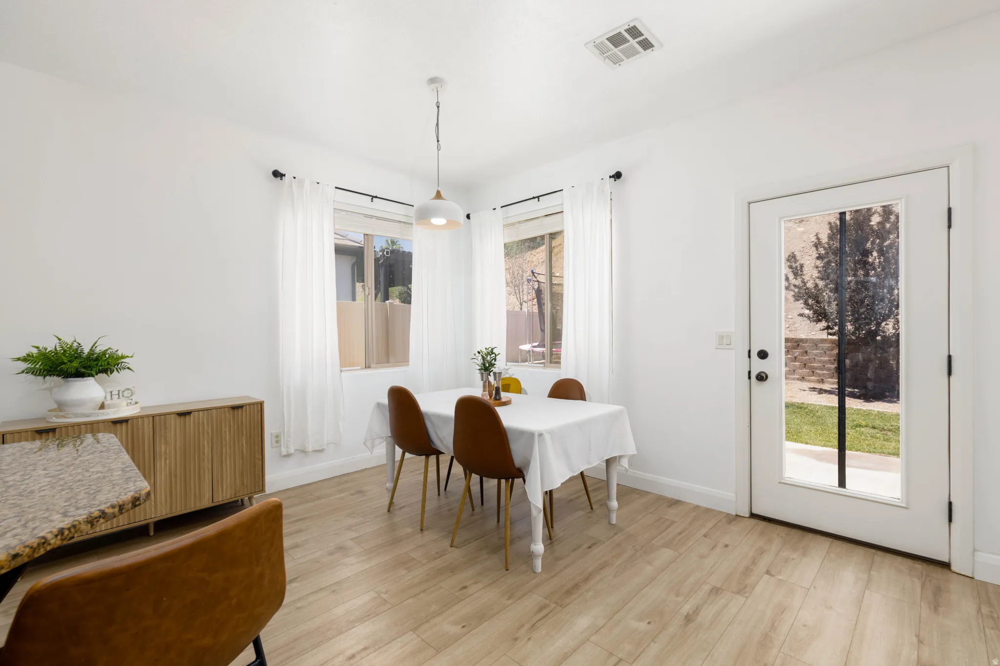 Bright dining area with wood-finish flooring, white walls, and a contemporary pendant light fixture