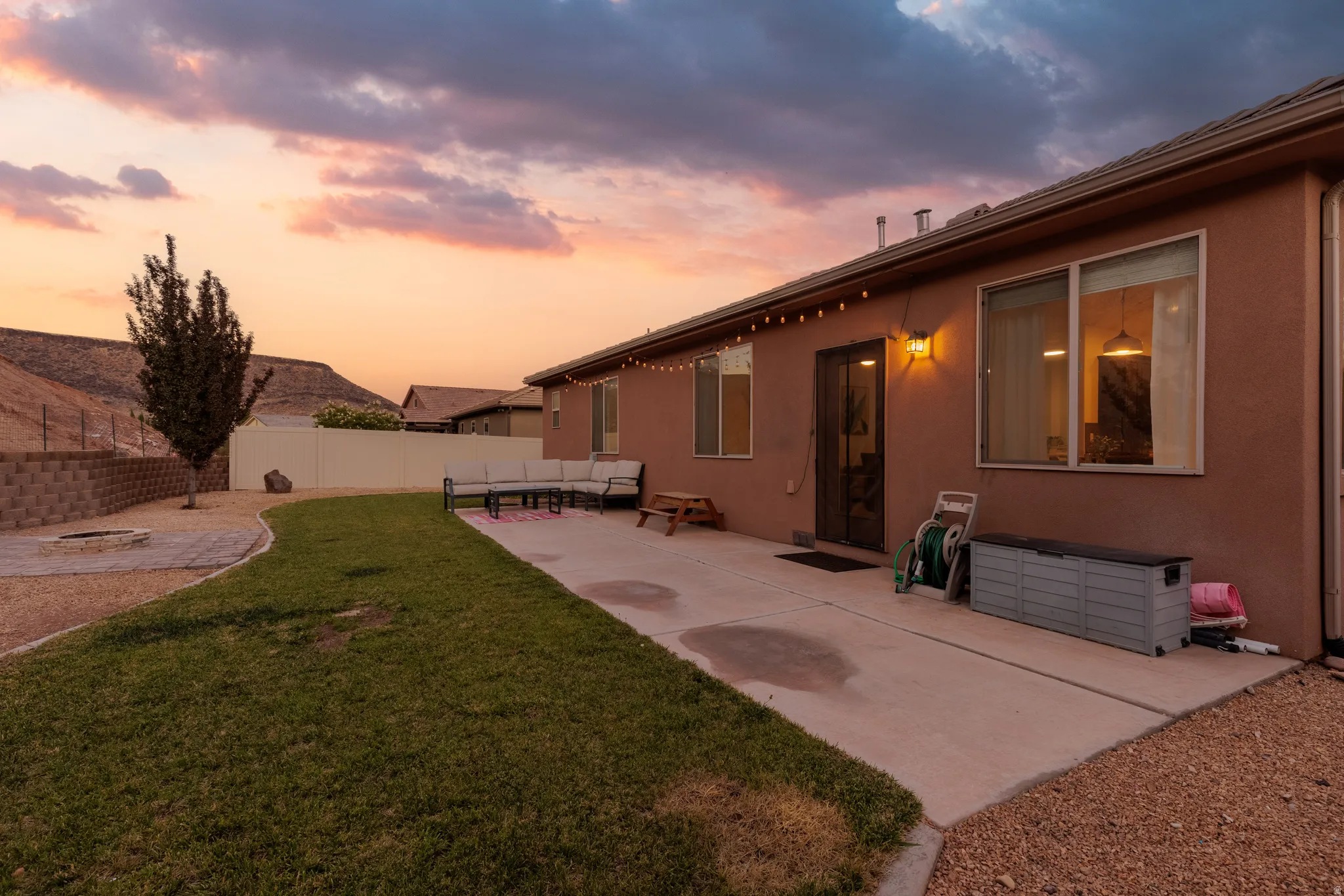 Expansive backyard featuring a concrete patio, a gravel fire pit area, a retaining wall, and a grass section