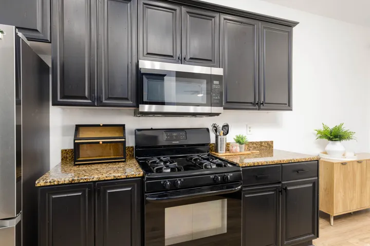 Kitchen featuring dark cabinetry, granite countertops, black gas range, and stainless steel microwave