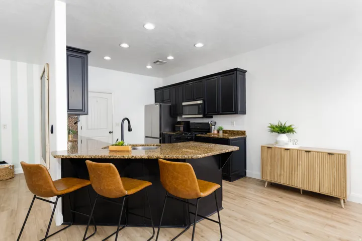Open-concept kitchen featuring black cabinetry, granite countertops, stainless steel appliances, and wood-finish flooring