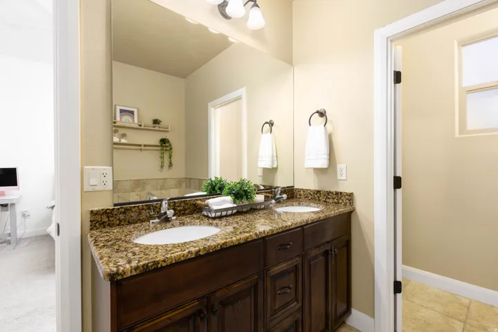 Primary suite bathroom featuring a dual sink vanity with a granite-style countertop, integrated sinks, and dark wood cabinetry