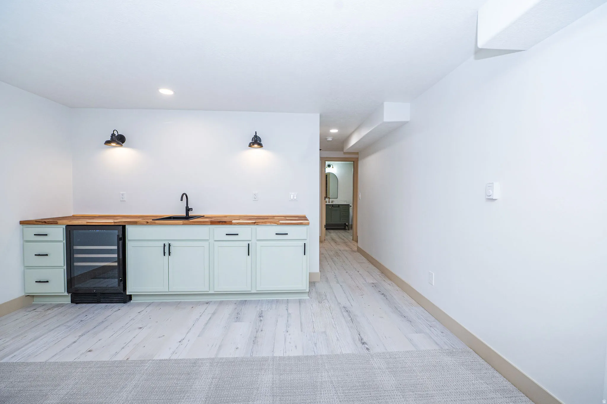 Built-in wet bar featuring sage green cabinetry, a black sink, wood-finish countertops, and an under-counter beverage refrigerator